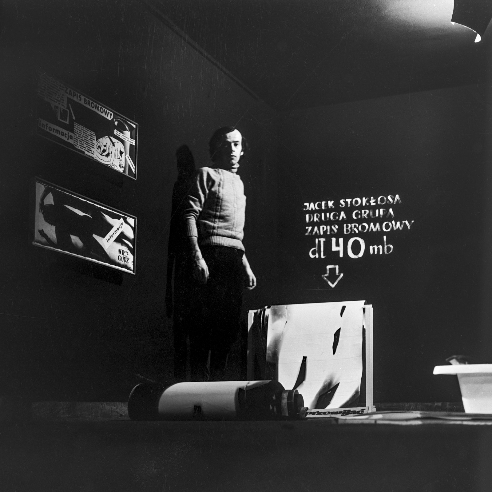 Zdjęcie mężczyzny w ciemnym pomieszczeniu, w tle napis Jacek Stokłosa Druga Grupa zapis bromowy