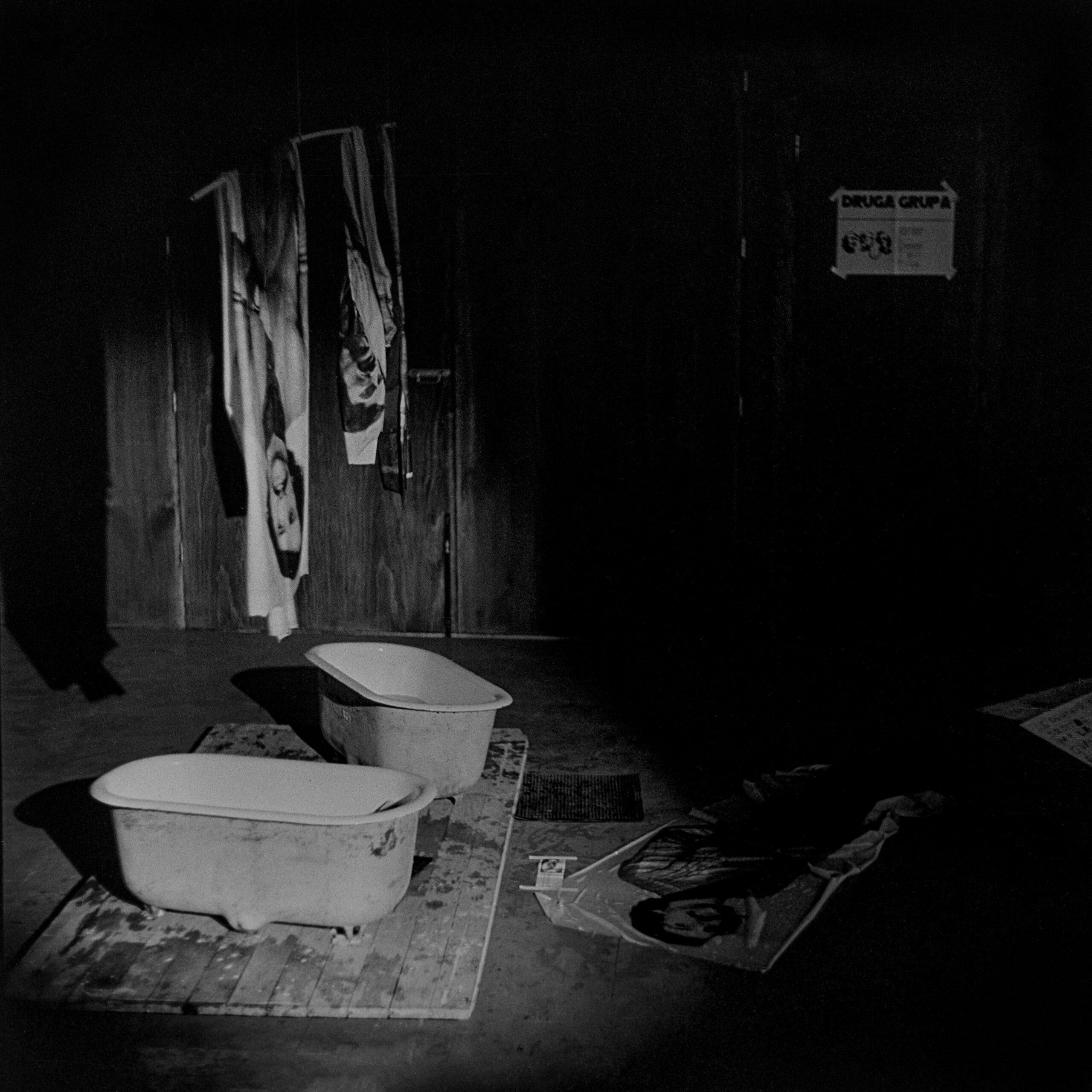 Archiwalne zdjęcie; wnętrze ciemnego pomieszczenia, na podłodze stoją małe wanienki do których skapuje woda z dużych odbitek