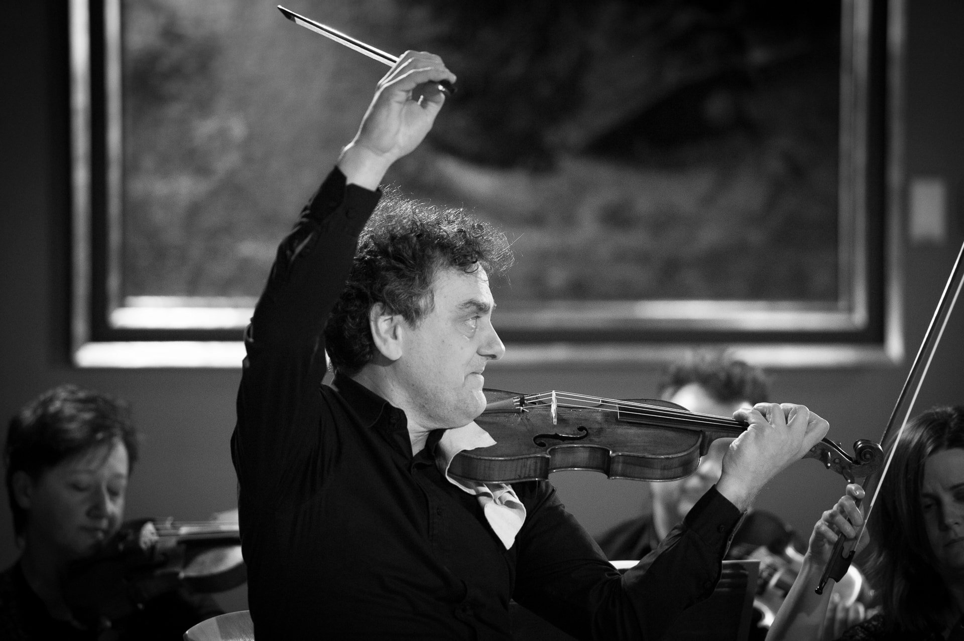 Mężczyzna grający na skrzypcach, z podniesioną do góry ręką trzymającą smyczek