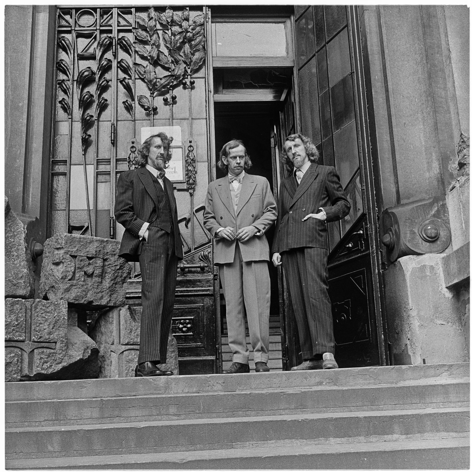 Archiwalne zdjęcie; trzech mężczyzn stoi przed wielkimi drzwiami do budynku