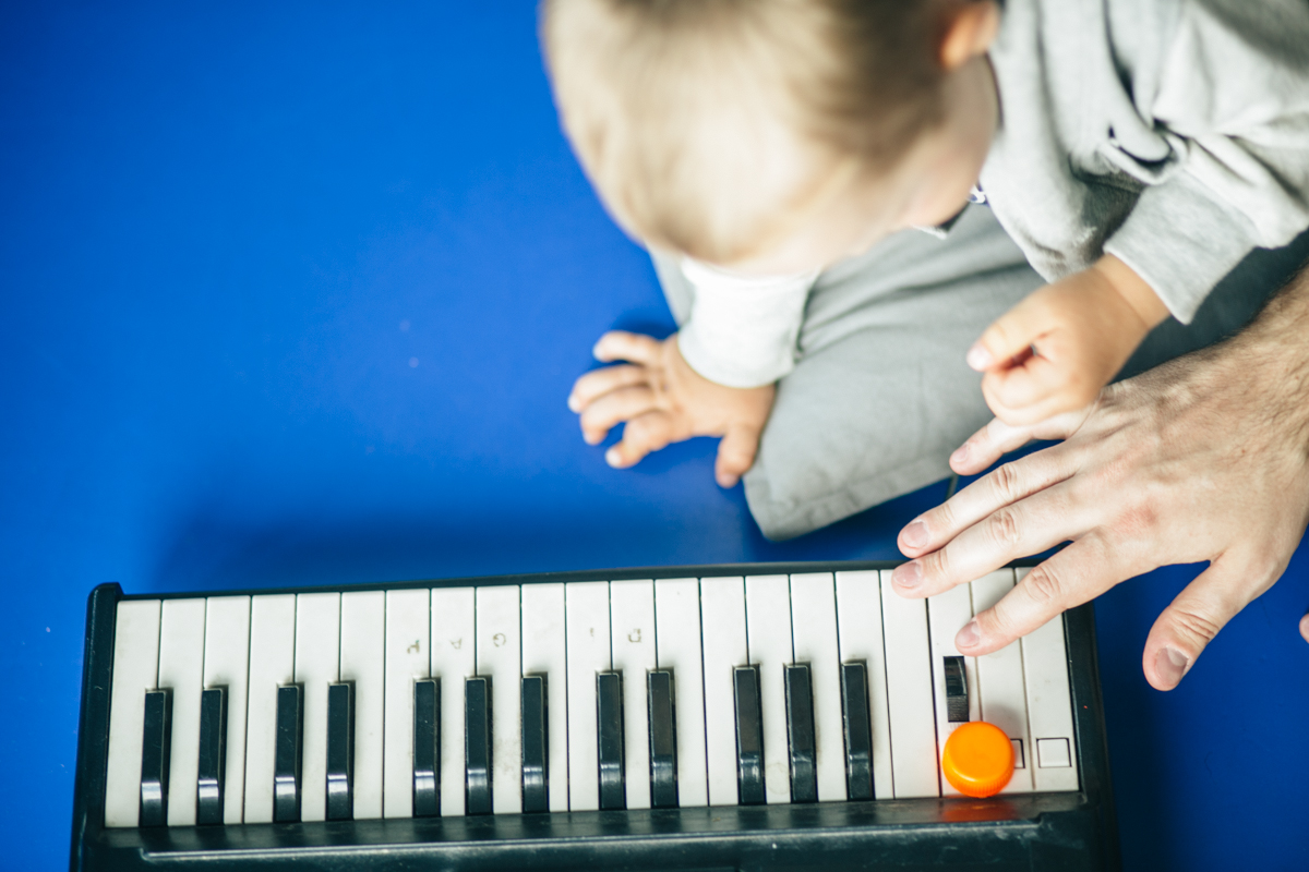 Na zdjęciu dziecko i ręka osoby dorosłej uderzająca w klawisze instrumentu.