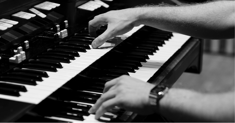 Zdjęcie przedstawia ręce ułożone na klawiszach fortepianu. 