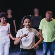 Kobieta w białej bluzce tańczy z uczestnikami warsztatów