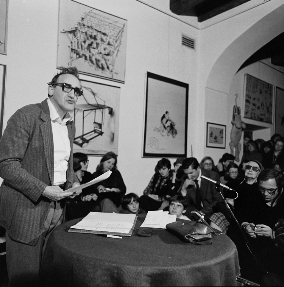 [Czarno-białe zdjęcie. Widać na nim przemawiającego Tadeusza Kantora oraz publiczność podczas otwarcia Ośrodka Teatru Cricot 2 w 1980 roku.]