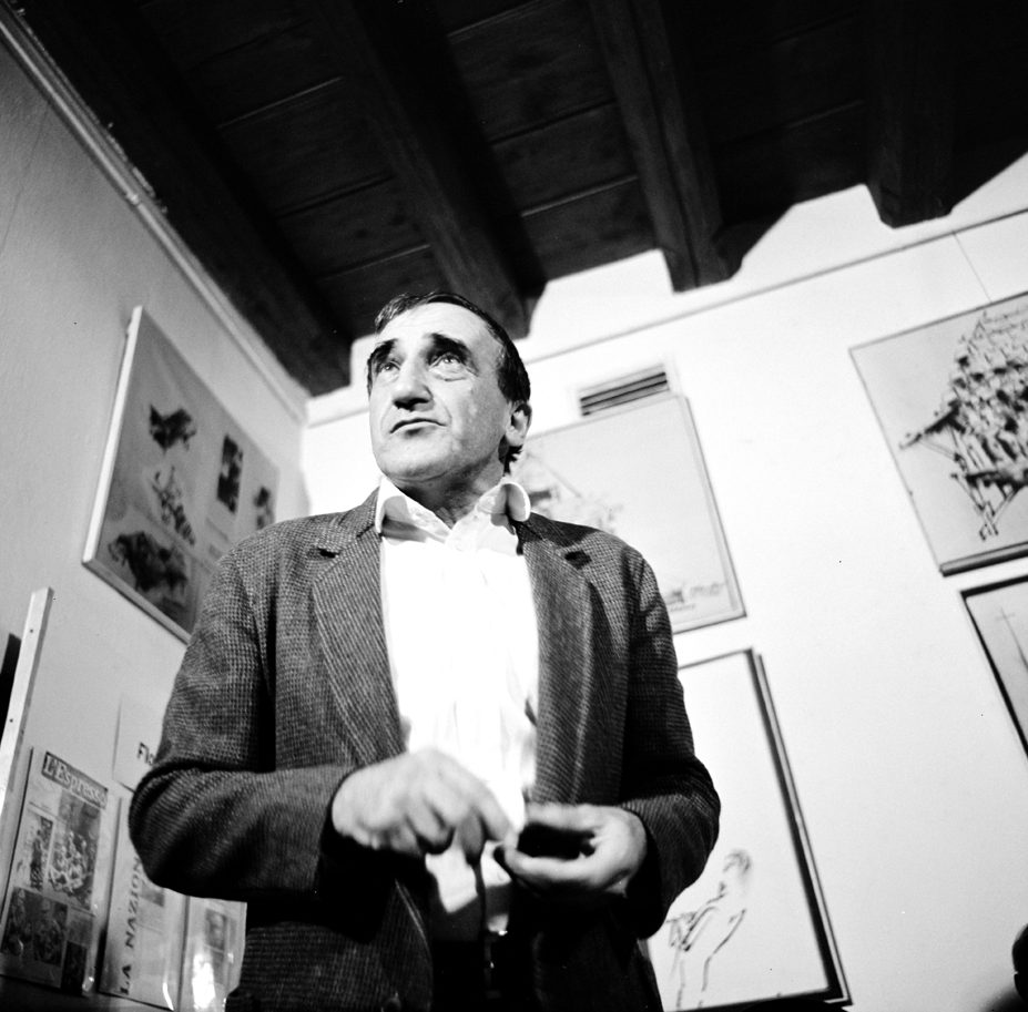 Czarno-białe zdjęcie Tadeusza Kantora w dniu otwarcia Cricoteki w 1980 roku. W tle na ścianach obrazy i wycinki z gazet.