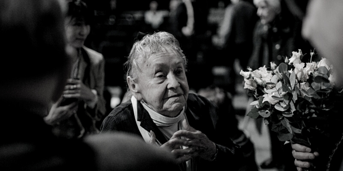 Czarno białe zdjęcie starszej kobiety trzymającej kwiaty.