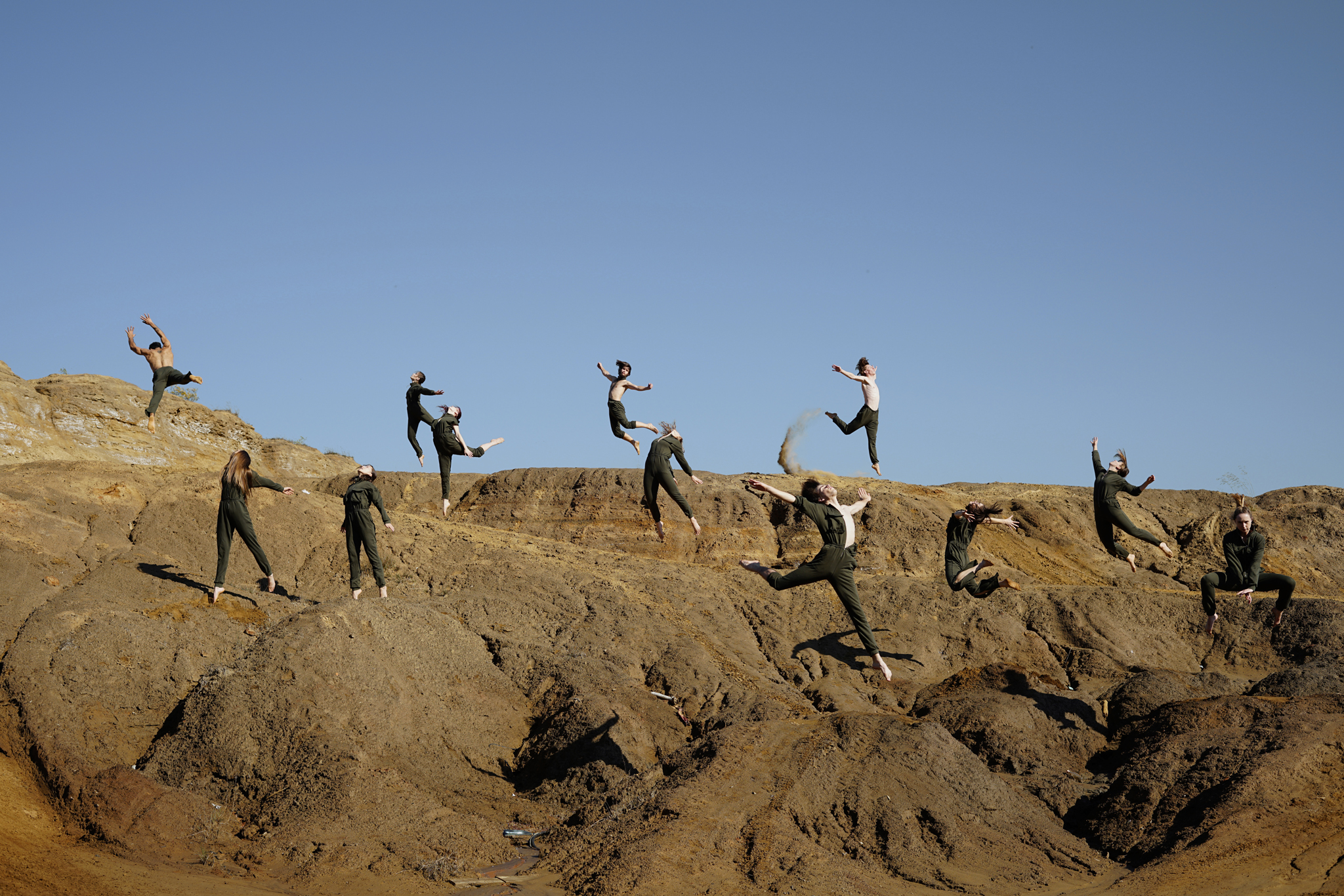 Grupa osób w roboczych kombinezonach stoi na hałdach ziemi.