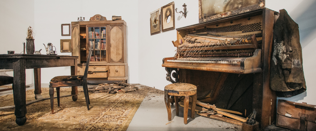 Wnętrze wystawy: przestrzeń przedstawia zniszczony pokój, z nadpalonymi meblami i uszkodzonymi przedmiotami.