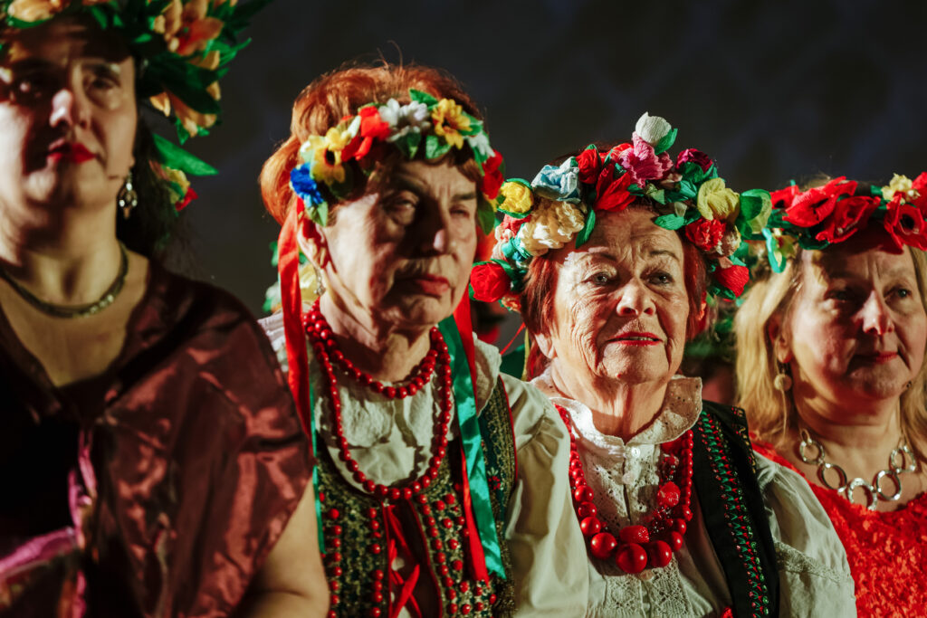 Zdjęcie ze spektaklu „Wesele po krakowsku”. Na zdjęciu cztery kobiety, widoczne od pasa w górę. Aktorki są ubrane w tradycyjne krakowskie stroje, korale i wianki.