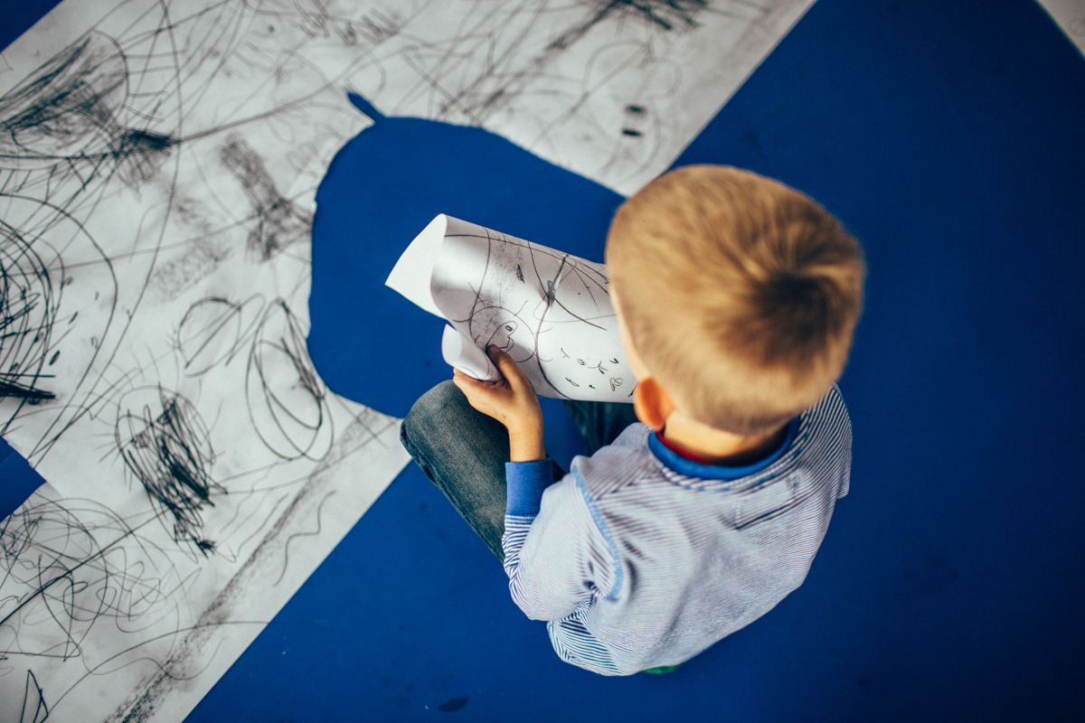 zdjęcie przedstawia dziecko w wieku 2-3 lat, widziane od góry, które ma w ręku pomalowany karton