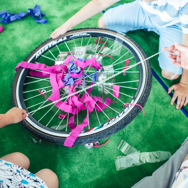 Zdjęcie przedstawia osoby bawiące się kołem od roweru, kolorowymi wstążkami, foliami...