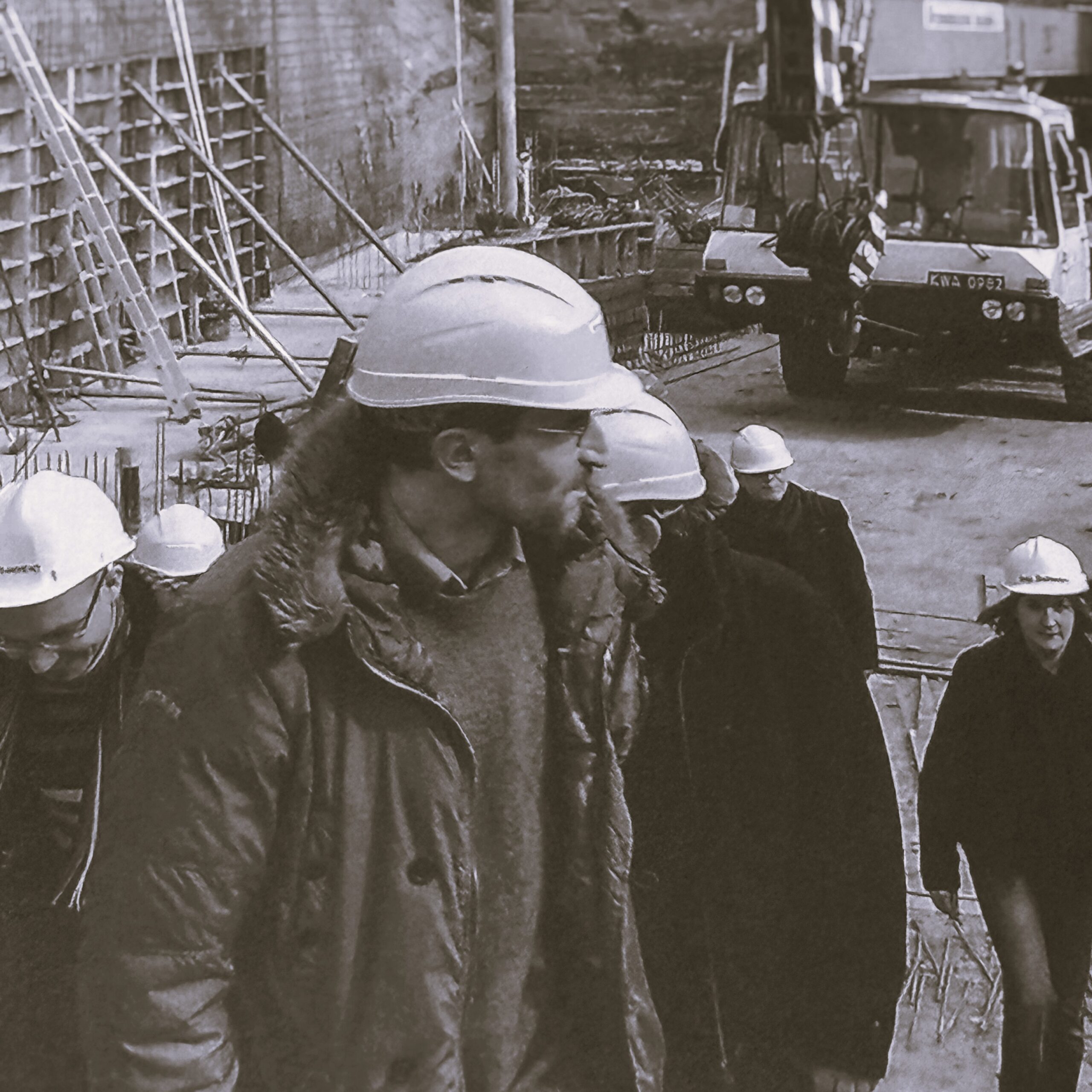 W centrum czarno-białej fotografii widoczny Stanisław Pochwała w kasku budowlanym. W tle budowa budynku Cricoteki - wykopy pod fundamenty i maszyny budowlane oraz kilka osób również w kaskach.