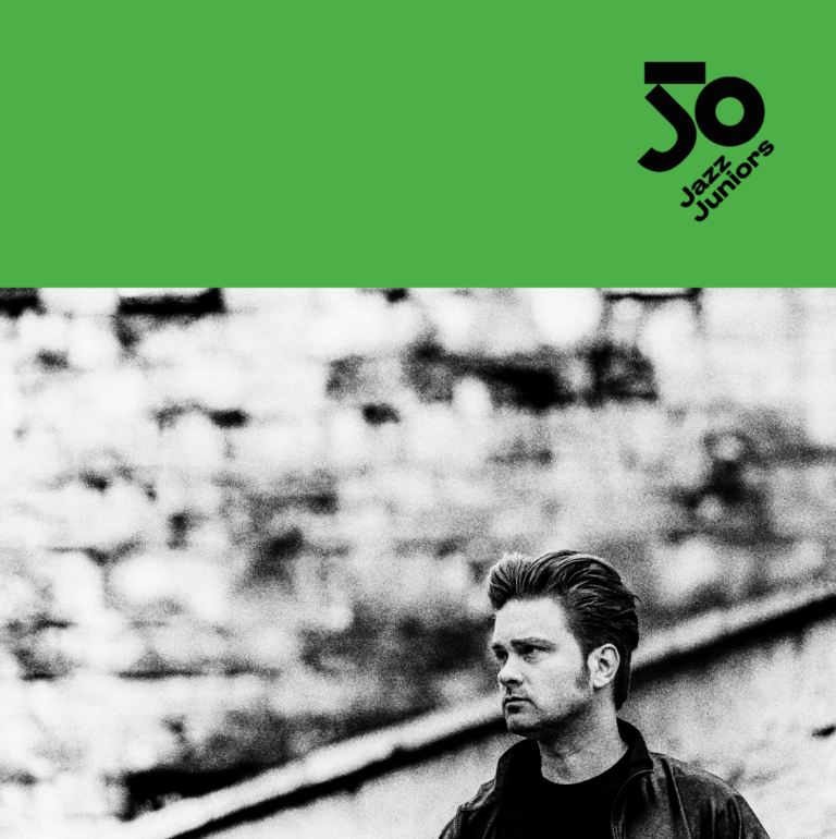Grafika festiwalu 50 Jazz Juniors. Górna część w jaskrawo zielonym kolorze z czarnym logo 50 Jazz Juniors w prawym rogu. Dolna część to czarno-białe zdjęcie młodego mężczyzny z zaczesanymi do tyłu włosami, ubranego w ciemną kurtkę. Mężczyzna patrzy w lewo, w tle rozmyty mur z cegły.